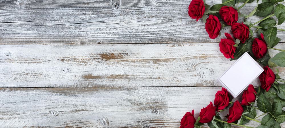 Valentine’s Day small gift box with a dozen red roses on wood
