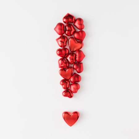 Exclamation mark made of red foil hearts on light background