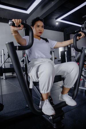 Dedicated young woman using chest press machine in modern gym