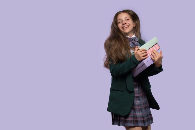 Smiling schoolgirl holding gift boxes in uniform.