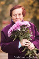 Portrait of older woman in purple coat holding bouquet of purple flowers bGXda0