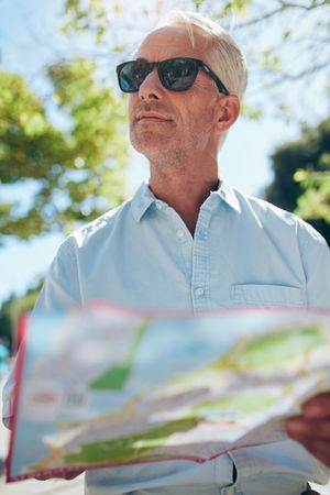 Close up shot of a mature man with a map standing outdoors in the city on a summer day