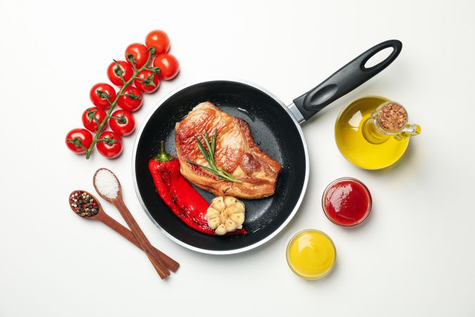Pan with fried steaks and ingredients for cooking on blank background, top view