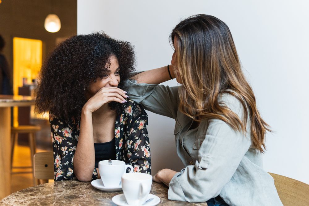 Smiling diverse girlfriends interacting at table in coffee house