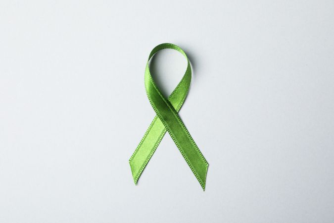 Green awareness ribbon on grey background, space for text