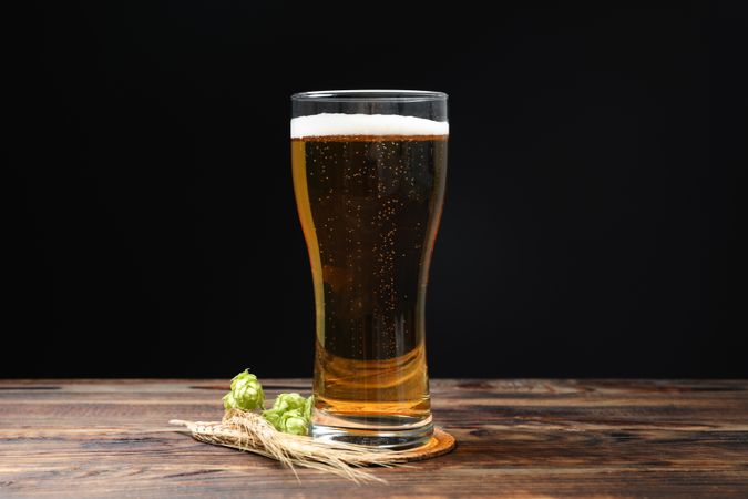 Mug with beer, spikelets and hop on wooden table, space for text
