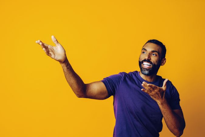 Black man smiling in yellow studio with hands up to the side