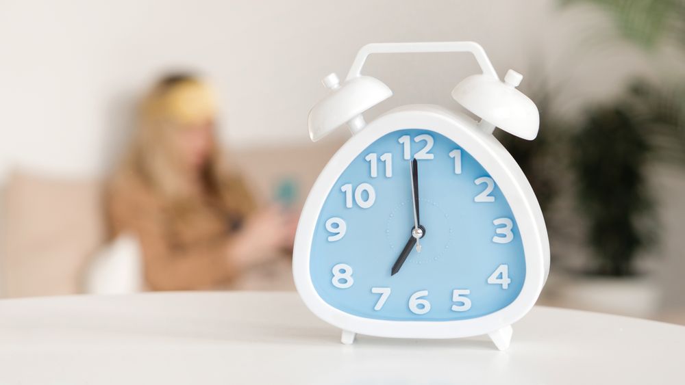 Alarm clock foreground, woman blurred in background.