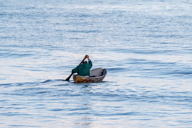Man in green shirt paddling in the middle of the ocean
