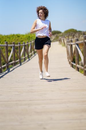 Fit sportswoman jogging along wooden path on sunny day
