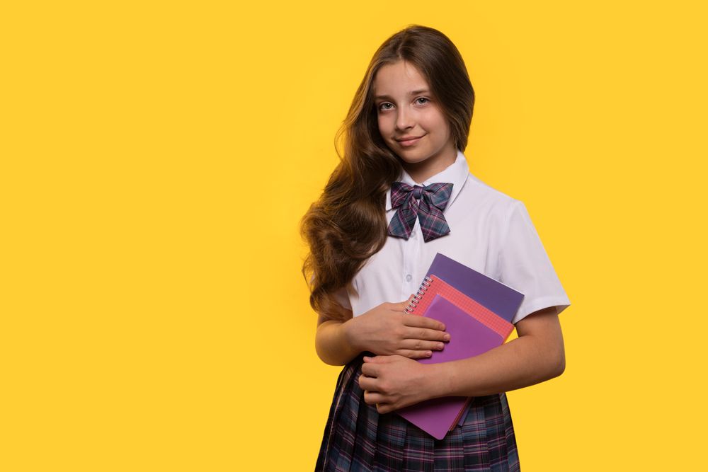 Schoolgirl holds colorful notebooks while posing confidently.