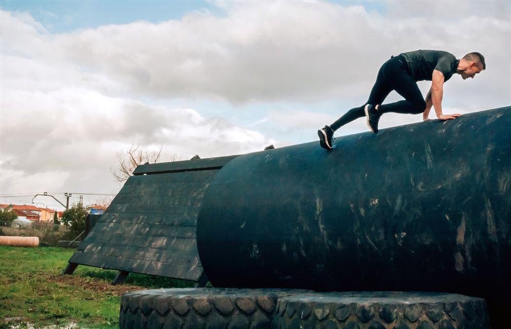 Man in an obstacle course climbing a drum