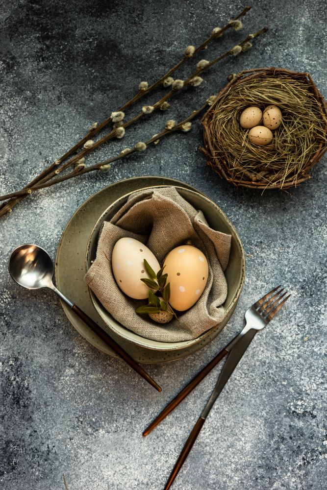 Top view of Easter holiday table setting with bowl of eggs and branch