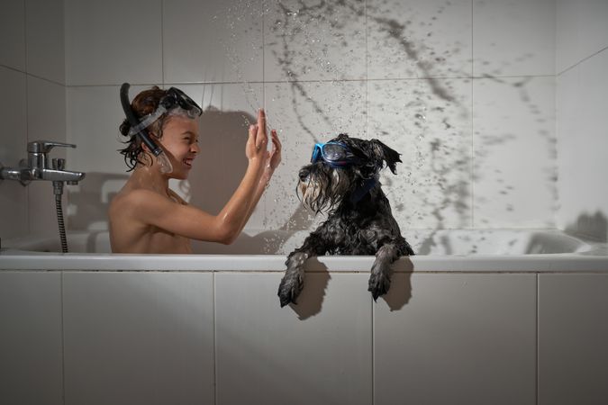 Smiling boy splashing water in tub with dog