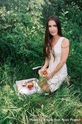 Woman in light dress kneeling on grass beside textile with fruit slices bEdMl4