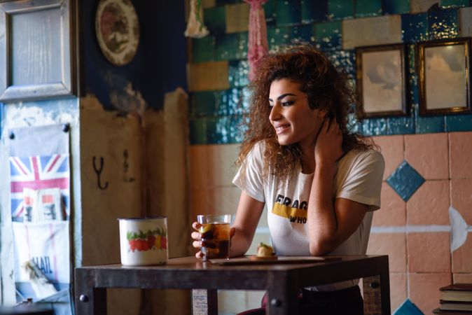 Arab woman in casual clothes smiling and looking wistfully in the distance with soda at restaurant