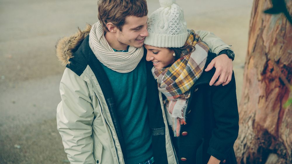 Smiling couple in winter coats embracing under tree