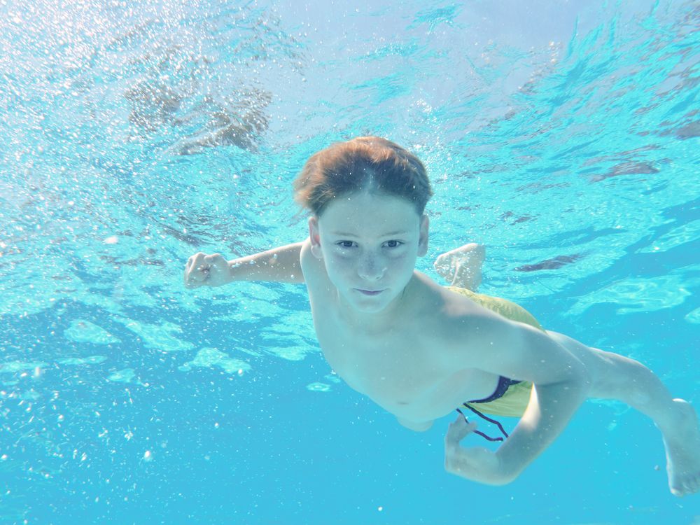Funny boy swimming underwater looking at camera