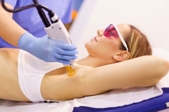 Client in protective glasses having laser hair removal treatment underarm at clinic