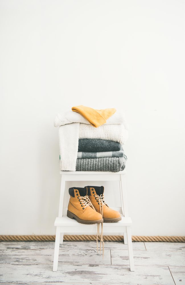 Pile of folded sweaters on light background with yellow boots, vertical composition, copy space