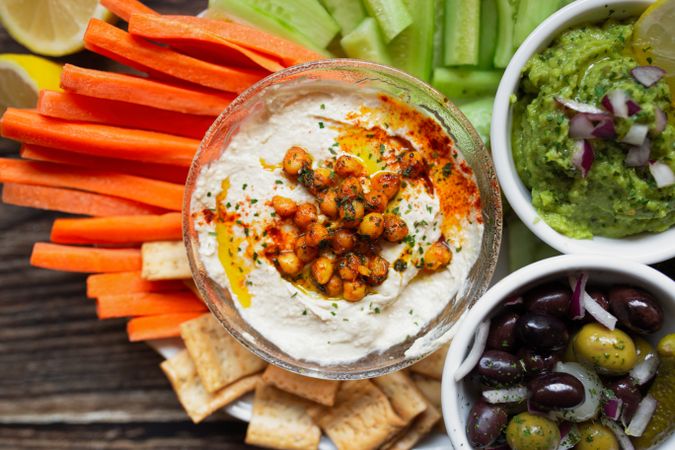 Tasty hummus and sauces decorated with bright cut vegetables on table