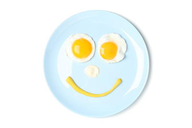 Looking down at blue plate with smiley face on it made of eggs and condiments