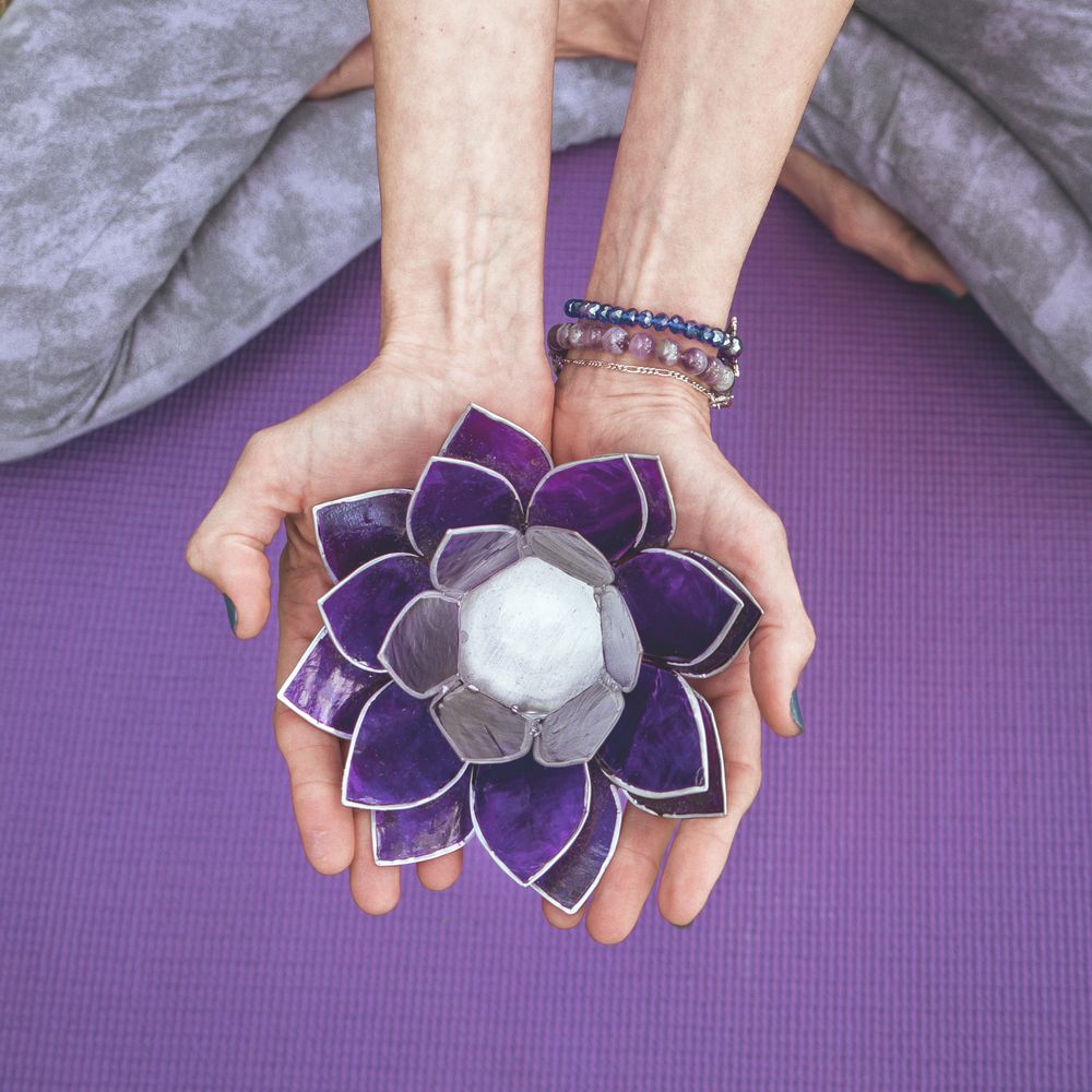 Top angle view of hands holding a purple glass lotus.  Yoga and meditation concept.