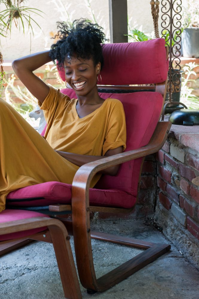 Woman sitting near garden laughing with eyes closed while siting in lounge chair