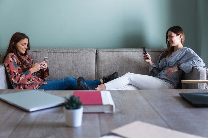 Young women resting on sofa and browsing smartphones