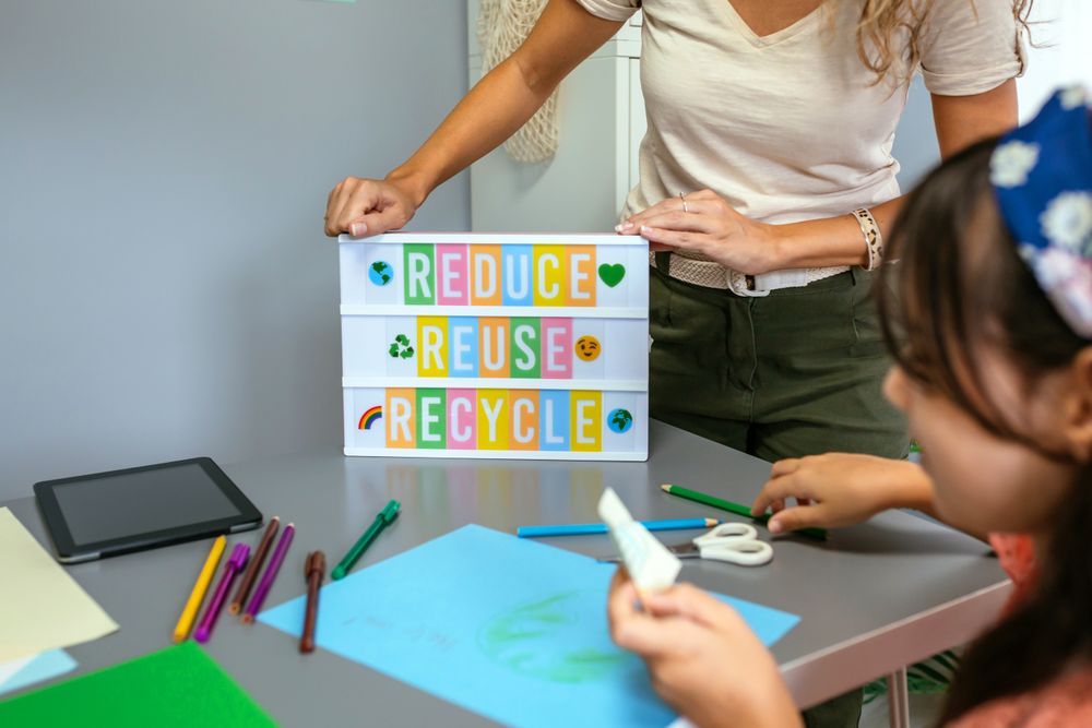 Teacher showing lightbox with text reduce, reuse, recycle while student drawing in classroom