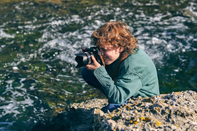 Positive boy taking photo near flowing water