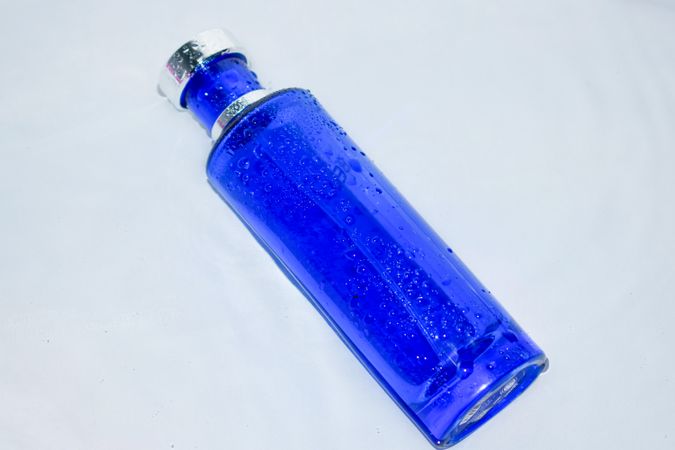 Blue perfume bottle with water droplets on light background with copy space