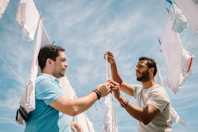 Multiracial men hanging clothes in bright day