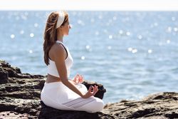 Side view of young woman stretching her back in lotus pose on rocky beach
