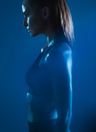 Strong young woman in sportswear standing against blue background