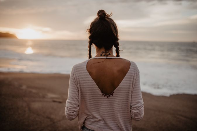 Anonymous female standing towards waving sea on sunset