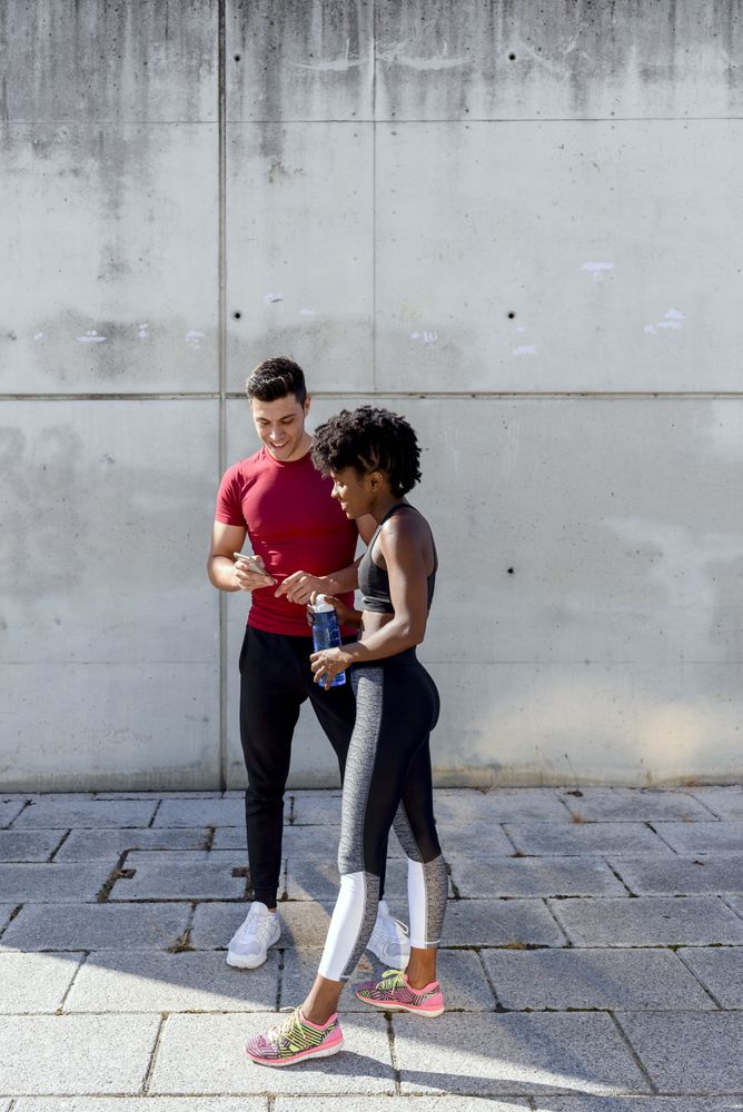 Multiracial sportive couple having break and using smartphone