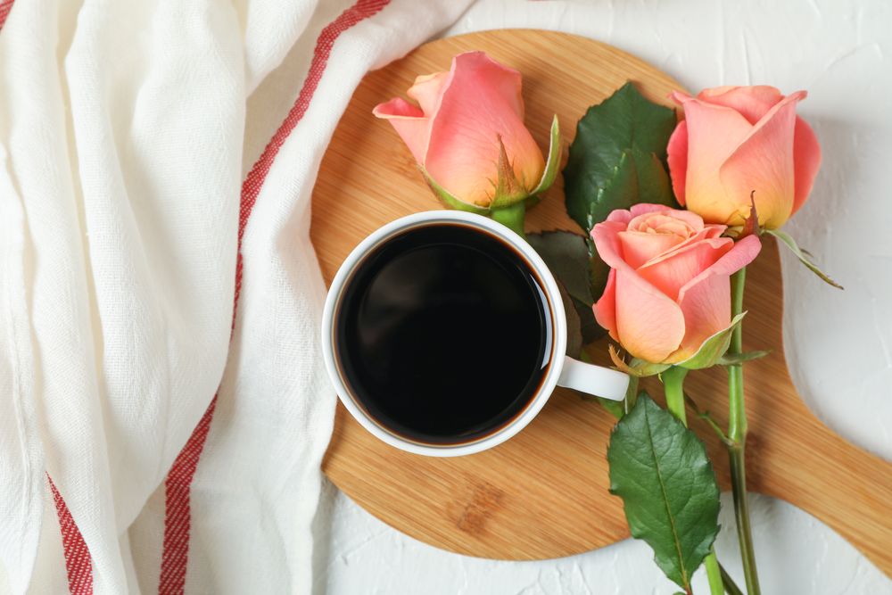 Composition with cup of coffee, roses and kitchen towel, top view
