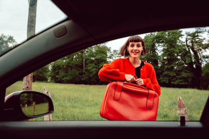 Woman putting suitcase in front window of car