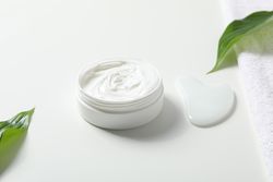 Jar with cream, leaves and gua sha on light background