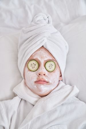 Kid with cucumber mask resting on bed at home