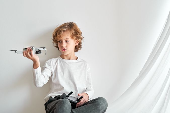 Cute boy with toy drone sitting against wall