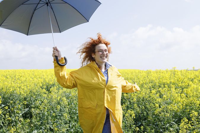 Joyful woman holding umbrella in yellow field