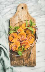 Mediterranean orange dish with onions, mint, and silver serving spoon on wooden board