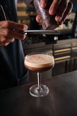 Barista decorating martini cocktail with grated chocolate in bar