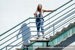 Smiling female in denim overalls standing on skateboard on stairs 4OVpZ5