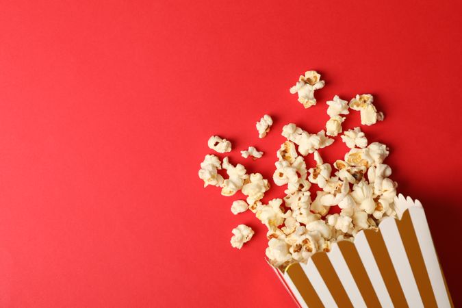 Flat lay composition with striped box and popcorn on color background