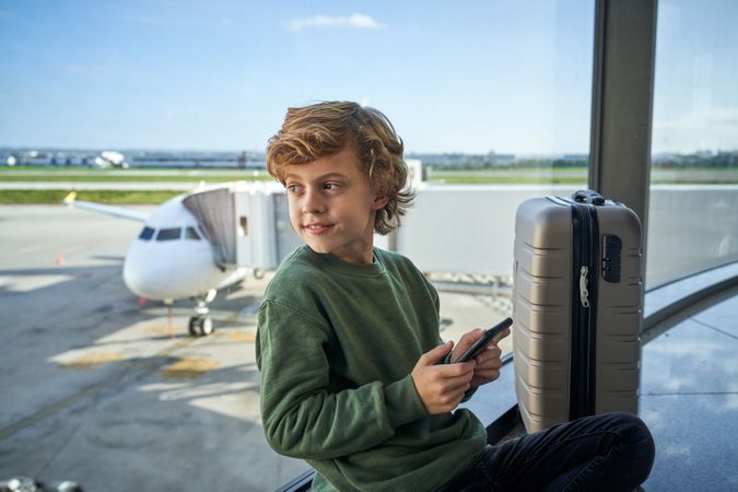 Smiling boy with smartphone and suitcase