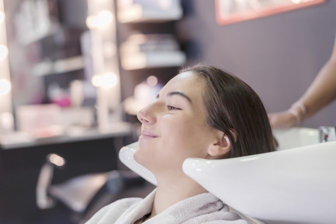 Female sitting with eyes closed and head back in sink at hairdressers awaiting a wash