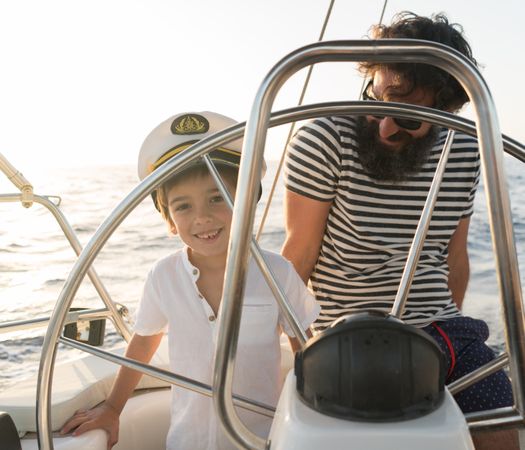 Man with boy holding steering wheel on yacht on water